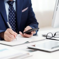 Cropped image of businessman checking messages in smartphone and taking notes in planner