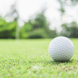 Golf ball on green with blurred pin flagstick and green tree background